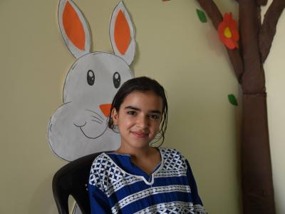 Tahani, 14, smiles while sitting inside a learning centre in Wadi Khaled, Akkar, with colourful handmade decorations behind her.