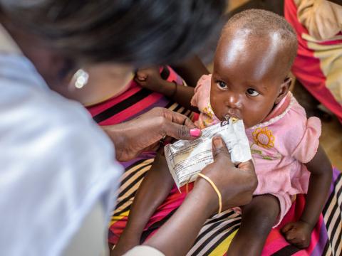 Little girl being fed by World Vision worker