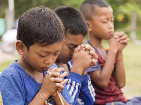 Three Khmer boys sitting with their finders locked and their eyes closed praying
