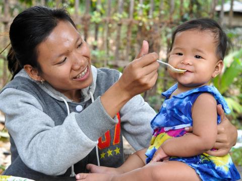 Khmer mum spoon feeds her child traditional Cambodian porridge nutritious food