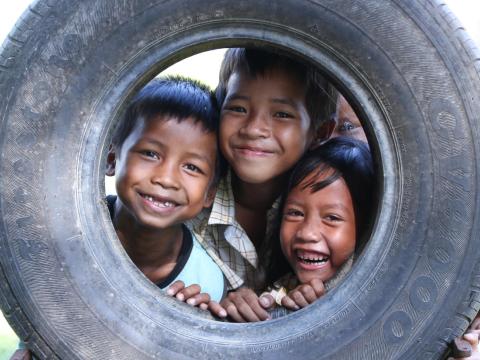 Three Khmer boys poke their heads through an old tire smiling at the camera
