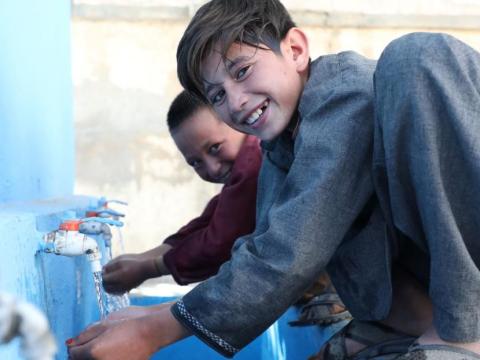 Children in Afghanistan collect water from water spouts