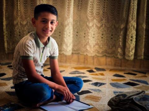 Muneer is writing his homework and prepared to go to his school with happy face that shows how glad he is.