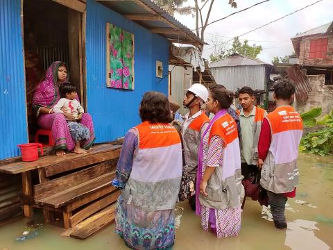Mukta and World Vision bangladesh youth led Disaster risk reduction team standing in knee-deep floodwater while speaking to a mother and child about their ongoing situation. 