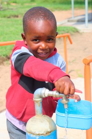 A Grade 1 learner fetching drinking water from one of the taps around his school.