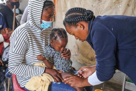 A community health working administers a vaccine to a child while her mother holds her