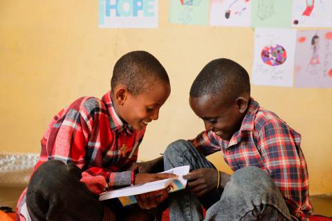 Bereket reading a book with his friend smiling