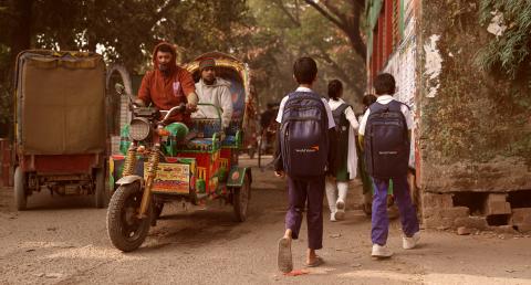 Children walk down a narrow, dusty street in Dhaka, Bangladesh, heading toward school.