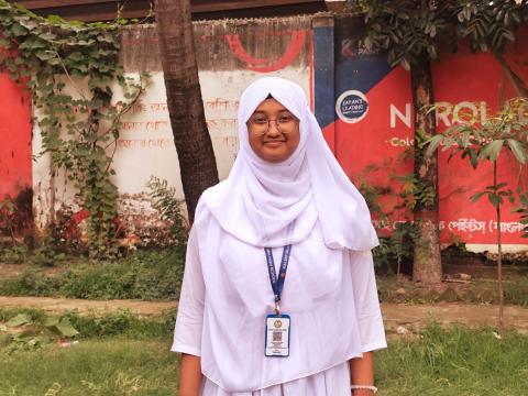 Tasnuva, a ninth-grade student in urban Dhaka standing Infront of her school