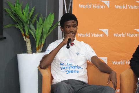 A teenage boy holding a microphone, seated on a chair.