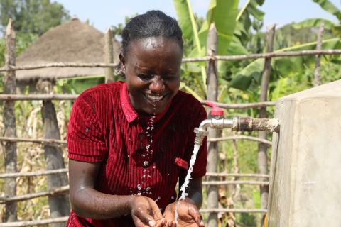A girl smiles while splashing water in her face at a local tap