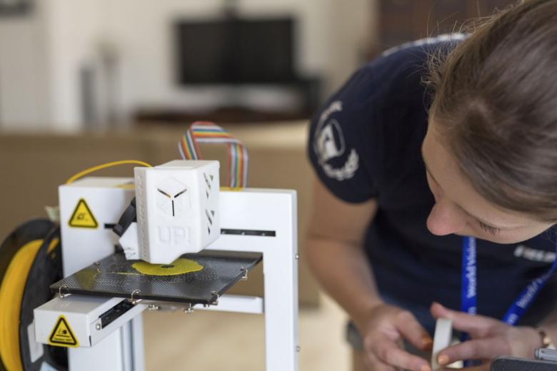 Woman looks as a 3D printer prints using yellow plastic