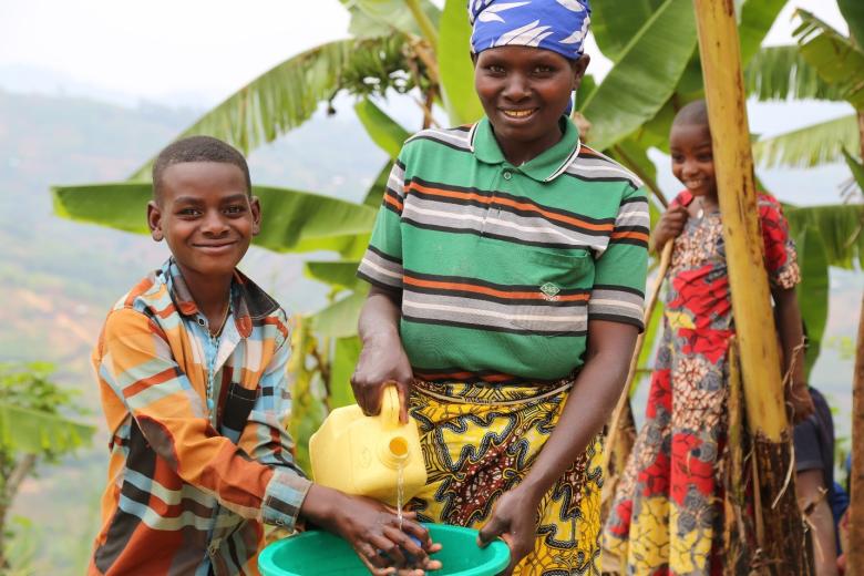 Photo summary: Josephine is pictures with her son, practicing proper and washing skill using flowing water and soap. This was taught to them through the WASH behavioral change messaging through different channels, including radio and training workshops.