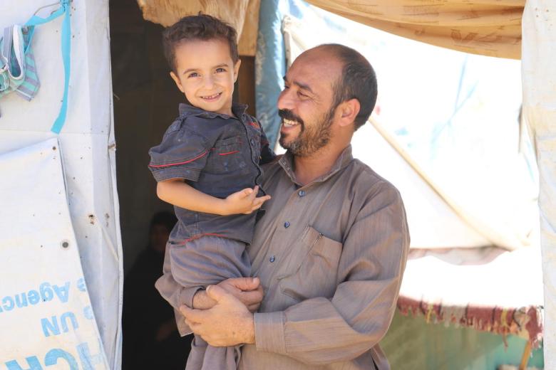 Syrian refugee Ayman in front his tent with his child