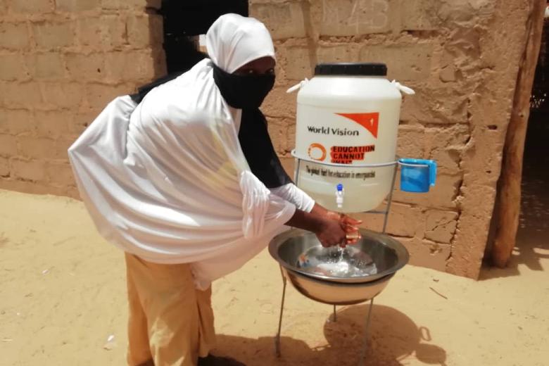 A girl washing her hands near a hygien kit provided by WV