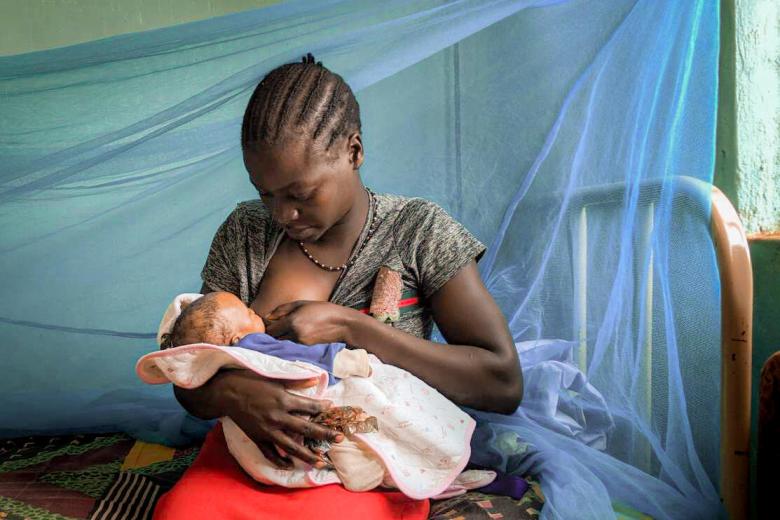 Mother in South Sudan breastfeeds her child against a mosquito net backdrop