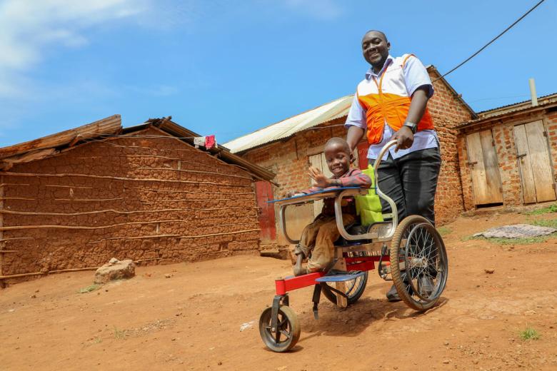 A World Vision Uganda staffer stands behind a child in a wheelchair