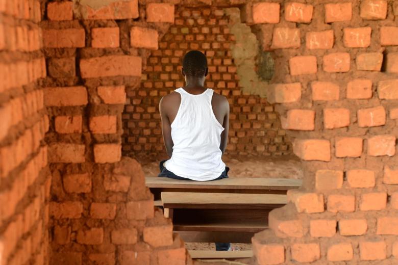 A former child soldier from South Sudan sits framed by a whole in the wall