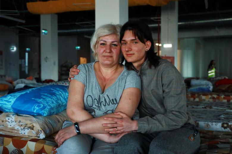 Evhen and his mother sit on a cot bed in a refugee center