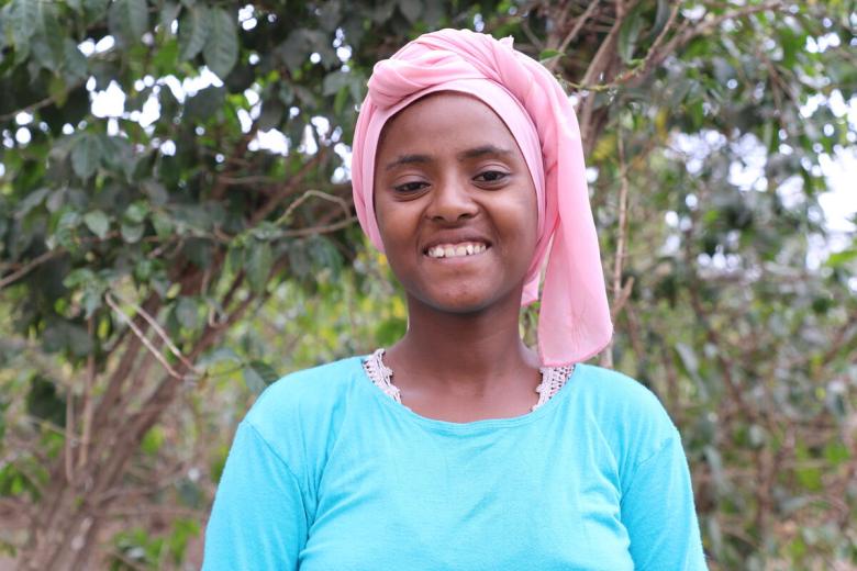 Semira smils for the camera wearing a blue shirt and pink head scarf