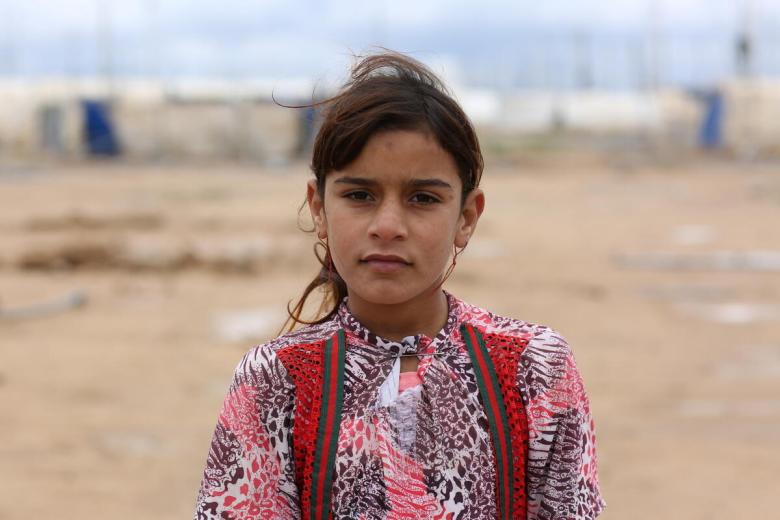 a young girl stands outside a refugee camp