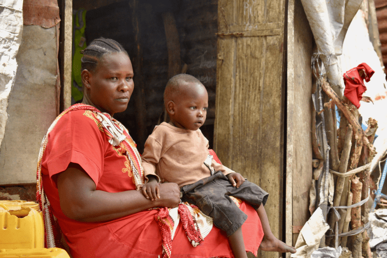 Angelina sits outside her hut with a child on her lap