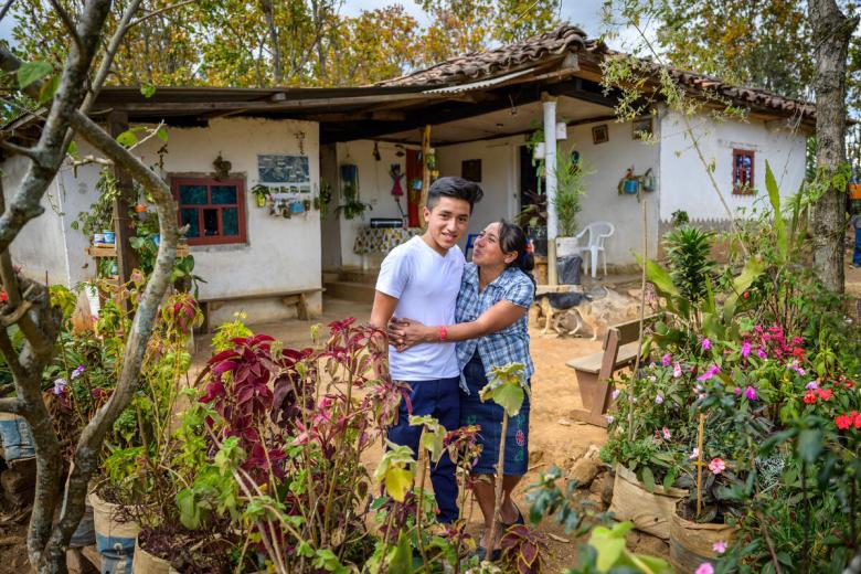 Mother of sponsored child stands in front of their home with her son