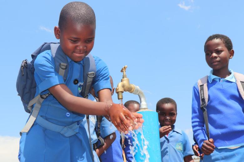 Children in eswatini washing under a tap