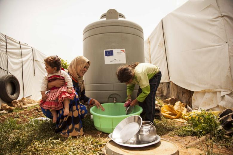 A family wash dishes at a water tank in a informal refugee settlement in Lebanon's Bekaa Valley.