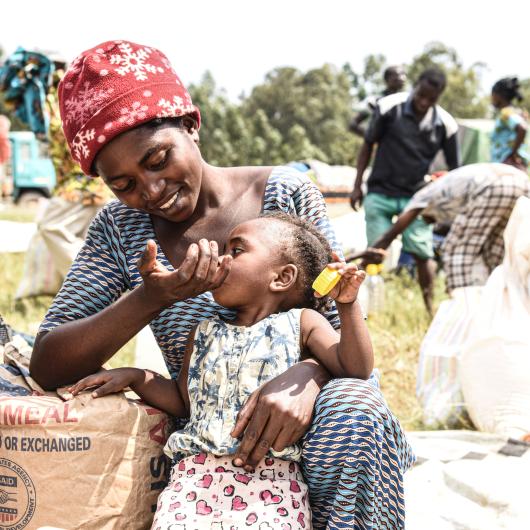 Une femme donnant à manger à son enfant dans un site de distribution des vivres