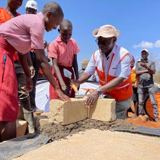 World Vision Kenya National Director and a pupil lay the foundation for the construction of a secondary school in Aroket