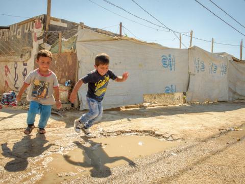 Two boys jumping in puddles at refugee camp