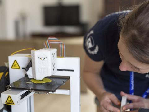 Woman looks as a 3D printer prints using yellow plastic