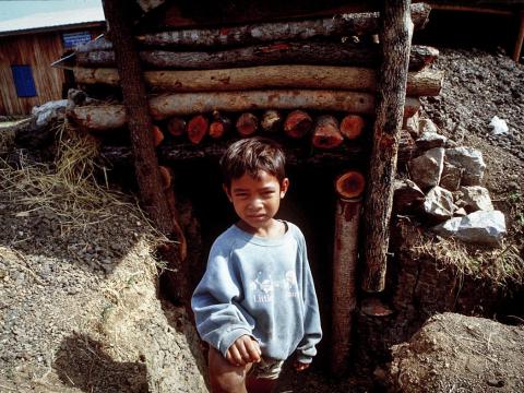 Young Khmer boy stands outside bomb shelter in rural Cambodia province.
