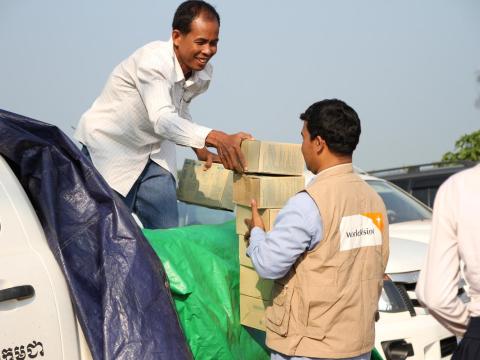 Two men from the World Vision emergency response team unload food supply boxes from the back of a white ute