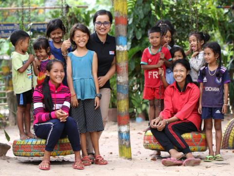Khmer girl stands with World Vision Cambodia staff member and other children from her community 