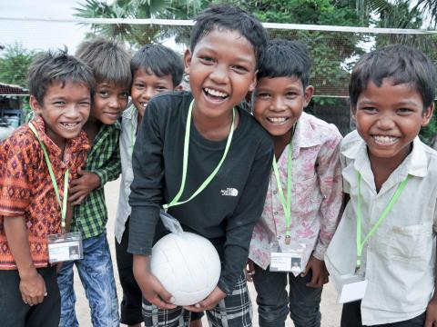 Group of three Khmer boys all smiling and laughing on outdoor volleyball court, Cambodia.