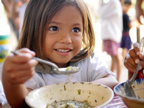 Khmer girl ginning as she holds spoon with nutritious porridge, Cambodia.