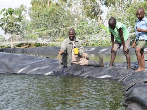 James feeding fish at one of his ponds with his sons. World Vision/Photo by Sarah Ooko.