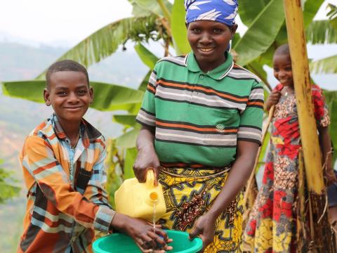Photo summary: Josephine is pictures with her son, practicing proper and washing skill using flowing water and soap. This was taught to them through the WASH behavioral change messaging through different channels, including radio and training workshops.