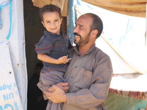 Syrian refugee Ayman in front his tent with his child