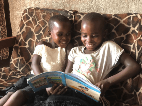 Kellen and her little sister happily reading a book they got from the reading camp