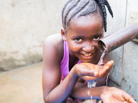 Young girl drinks clean water from the pipe in Sierra Leone