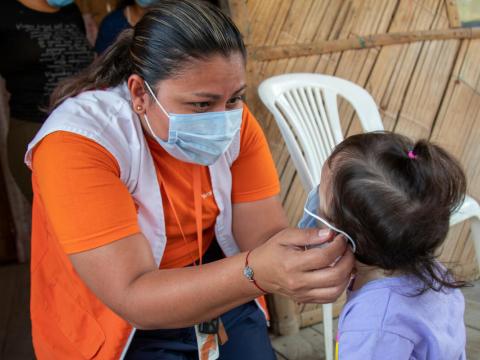 World Vision staff member helps child put on mask
