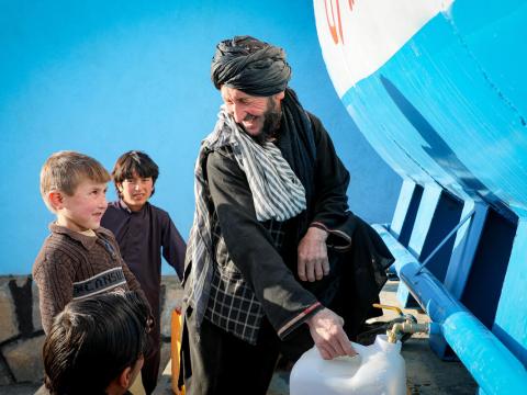 Man in Afghanistan helps children collect water from solar-powered water pump built with support from UNICEF