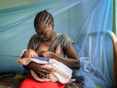 Mother in South Sudan breastfeeds her child against a mosquito net backdrop