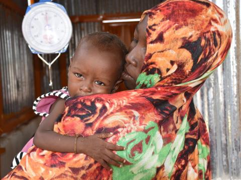 Hunger crsis pic, mother with young child in her arms near scale