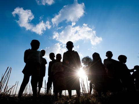 Children in silhouette stand beneath a blue sky in Africa