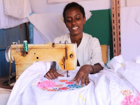 Woineshet Bekele smiling sitting on a sewing machine