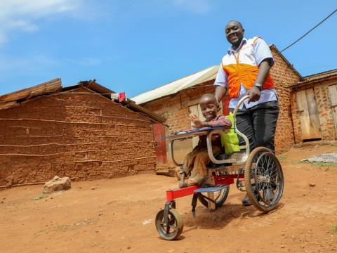 A World Vision Uganda staffer stands behind a child in a wheelchair 